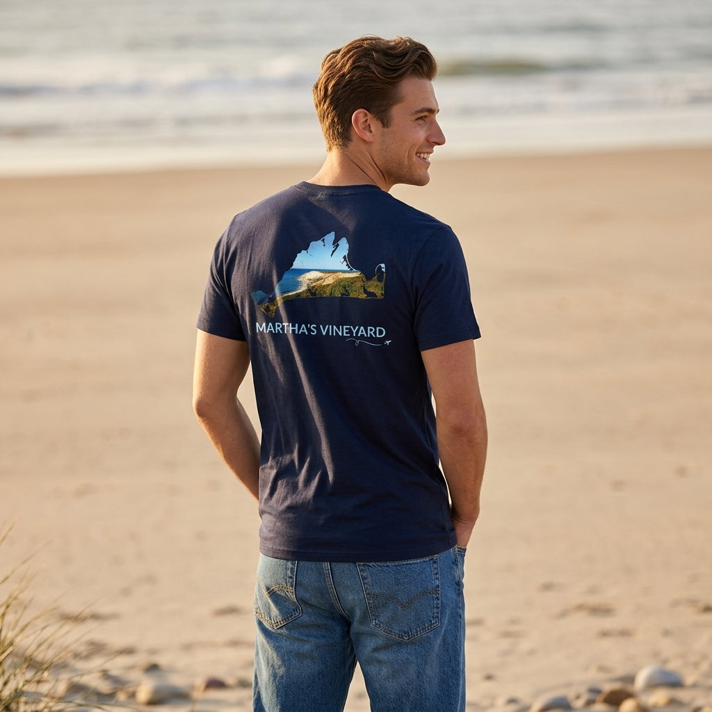Man wearing a navy Martha’s Vineyard t-shirt on the beach, with an Aquinnah Cliffs scene inside the island outline on the back