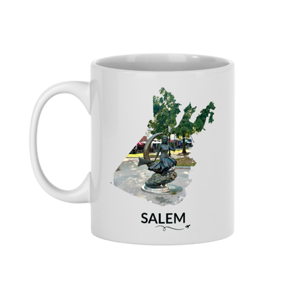 White 11 oz Salem mug featuring the Bewitched Sculpture inside the Salem outline, Salem lettering, and a small plane with a swirly line