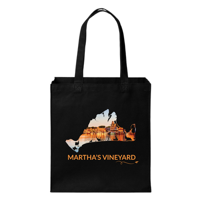 Black cotton canvas tote bag featuring a hand-drawn Martha's Vineyard outline filled with Oak Bluffs Harbor at sunset, with boats, waterfront buildings, and golden reflections on the water. The words "Martha's Vineyard" appear below the artwork with a small airplane icon and looping flight path.