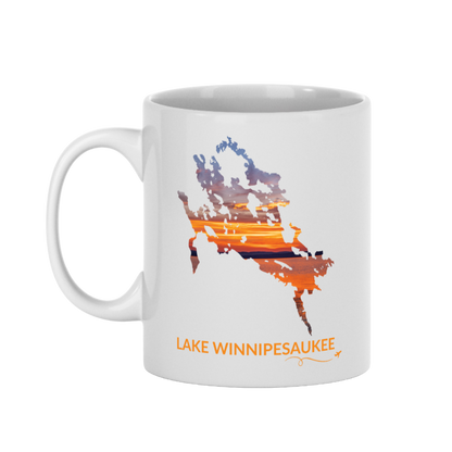 White 11 oz ceramic mug featuring a hand-drawn outline of Lake Winnipesaukee filled with a photograph of an orange and gold sunset captured on the lake. The words “Lake Winnipesaukee” appear below the artwork with a small airplane icon and looping flight path.