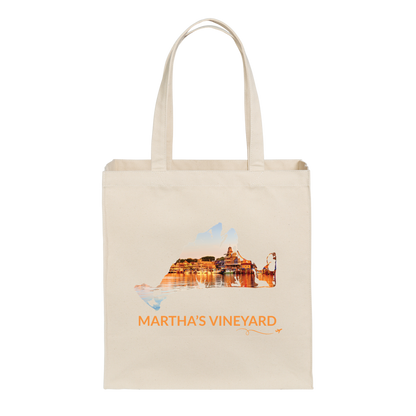 Natural cotton canvas tote bag featuring a hand-drawn Martha's Vineyard outline with Oak Bluffs Harbor at sunset, including boats, waterfront buildings, and shimmering reflections on the water. The words "Martha's Vineyard" appear below the artwork with a small airplane icon and looping flight path.
