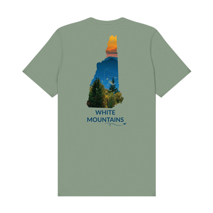 Sage t-shirt featuring a hand-drawn New Hampshire outline filled with a photograph of the White Mountains, with evergreen trees, layered mountain peaks, and an orange sunset sky. The words “White Mountains” appear below the artwork with a small airplane icon and looping flight path.