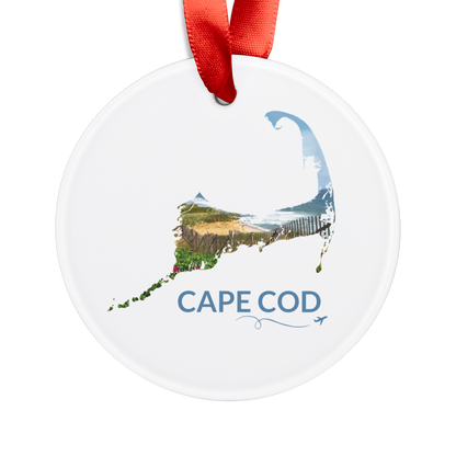 Round ceramic ornament featuring a hand-drawn Cape Cod outline filled with beach roses, weathered sand fencing, rolling dunes, and the Atlantic Ocean. The words "Cape Cod" appear below the artwork with a small airplane icon and looping flight path.