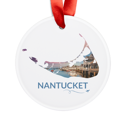 White Nantucket ornament with red ribbon featuring a harbor scene at sunset inside the island outline, blue Nantucket lettering, and airplane swirl