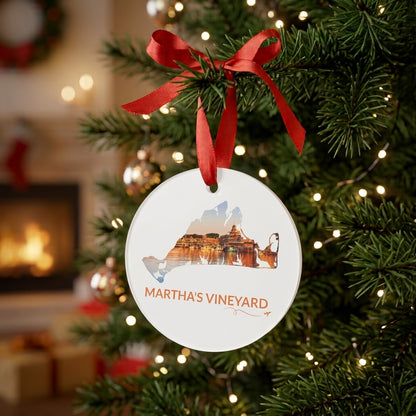 White Martha’s Vineyard ornament hanging on a Christmas tree with a red ribbon, featuring Oak Bluffs Harbor at sunset inside the island outline, orange Martha’s Vineyard lettering, and a small airplane with swirl