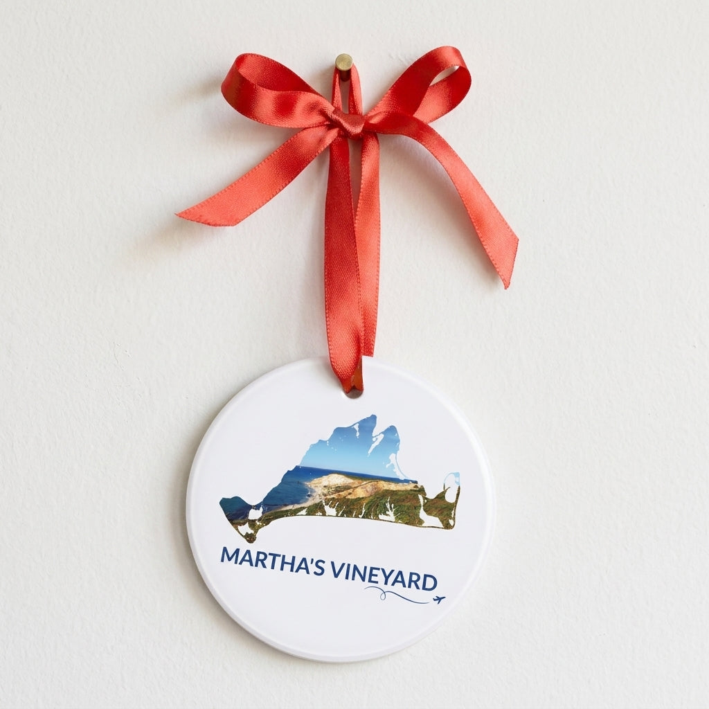 Martha’s Vineyard Aquinnah Cliffs ornament hanging from a red ribbon on a white wall, featuring the cliffs and coastline inside the island outline, blue Martha’s Vineyard lettering, and a small airplane with swirl