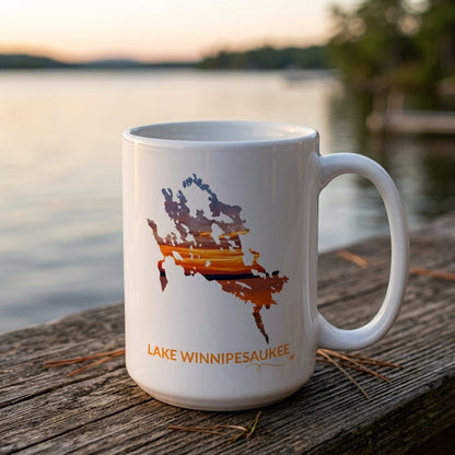 White Lake Winnipesaukee mug on a wooden dock at sunset, featuring a colorful sunset over the lake inside the lake outline, orange Lake Winnipesaukee lettering, and a small airplane with swirl