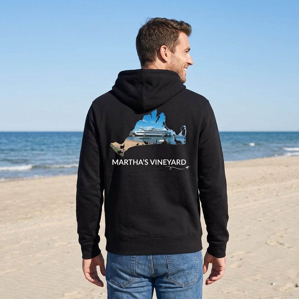 Man wearing a black Martha's Vineyard zip-up hoodie on the beach, showing the Steamship docked in Vineyard Haven inside a hand-traced island outline on the back