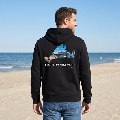 Man wearing a black Martha's Vineyard zip-up hoodie on the beach, showing the Steamship docked in Vineyard Haven inside a hand-traced island outline on the back