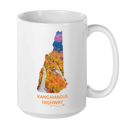 White 15 oz ceramic mug featuring a hand-drawn New Hampshire outline filled with a photograph of the Kancamagus Highway surrounded by colorful autumn foliage. The words "Kancamagus Highway" appear below the artwork with a small airplane icon and looping flight path.