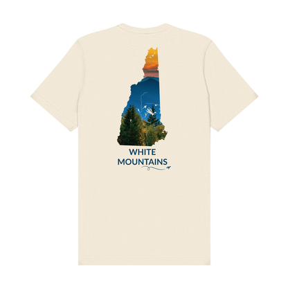 Natural t-shirt featuring a hand-drawn New Hampshire outline filled with a photograph of the White Mountains, with evergreen trees, layered mountain peaks, and an orange sunset sky. The words “White Mountains” appear below the artwork with a small airplane icon and looping flight path.