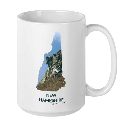 White 15 oz ceramic mug featuring a hand-drawn New Hampshire outline filled with a photograph of the Old Man of the Mountain. The words “New Hampshire” appear below the artwork with a small airplane icon and looping flight path.