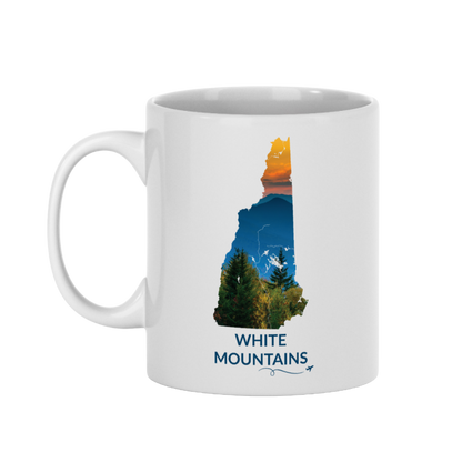 White 11 oz ceramic mug featuring a hand-drawn New Hampshire outline filled with a photograph of mountain peaks beneath an orange sunset sky. The words "White Mountains" appear below the artwork with a small airplane icon and looping flight path.
