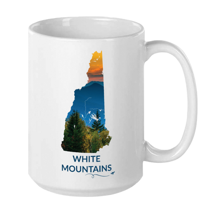 White 15 oz ceramic mug featuring a hand-drawn New Hampshire outline filled with a photograph of the White Mountains at sunset. The words "White Mountains" appear below the artwork with a small airplane icon and looping flight path.