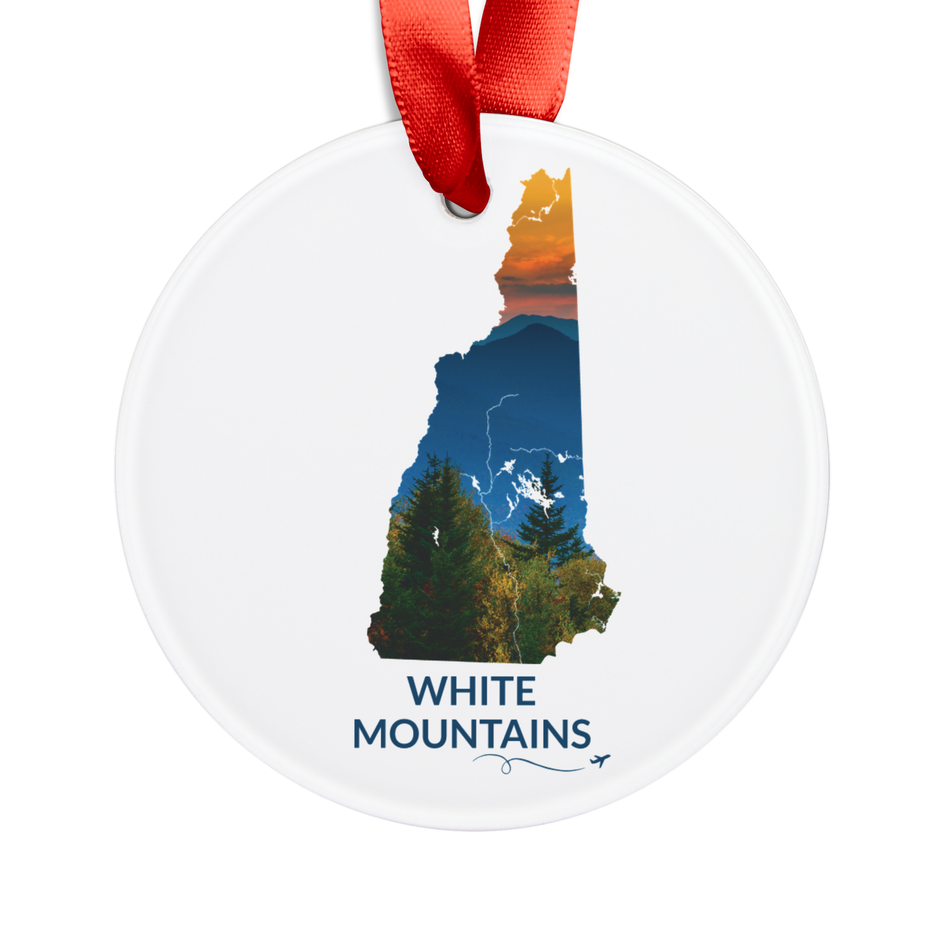 Round acrylic New Hampshire ornament featuring a hand-drawn state outline filled with a sunset photograph of the White Mountains. The words "White Mountains" appear below the artwork with a small airplane icon and looping flight path.